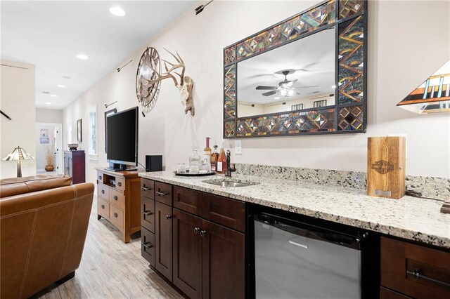 bar with light wood-style flooring, a ceiling fan, a sink, indoor wet bar, and dishwasher