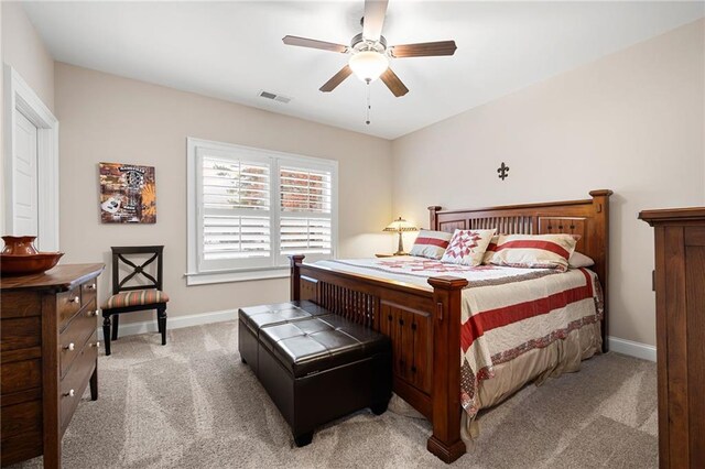 bedroom with visible vents, light colored carpet, baseboards, and ceiling fan