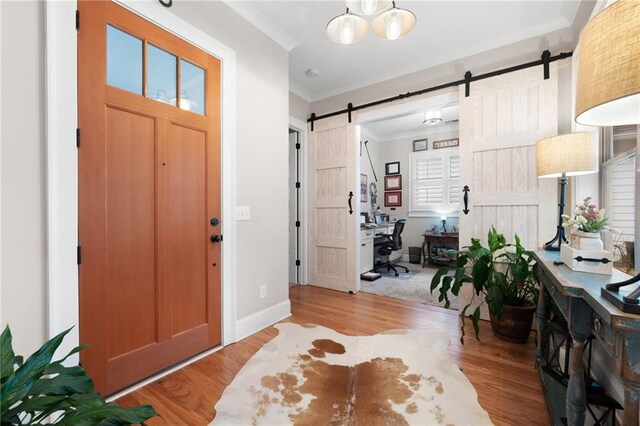 foyer with a barn door, a notable chandelier, wood finished floors, and crown molding