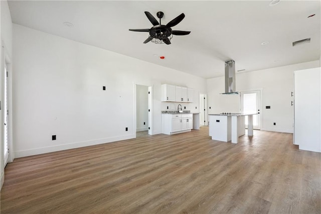 unfurnished living room featuring ceiling fan, sink, and light wood-type flooring