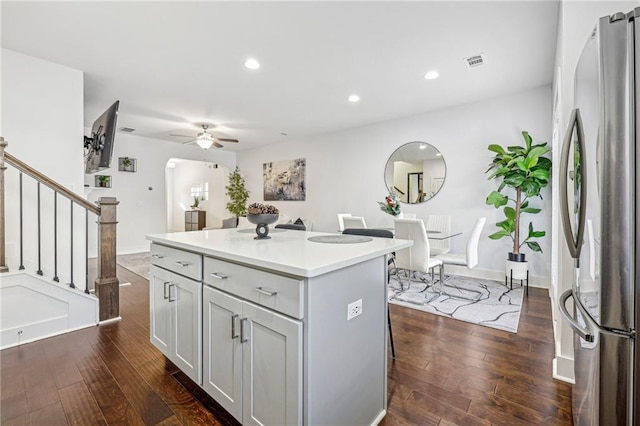 kitchen with ceiling fan, a center island, a kitchen breakfast bar, dark hardwood / wood-style flooring, and stainless steel fridge