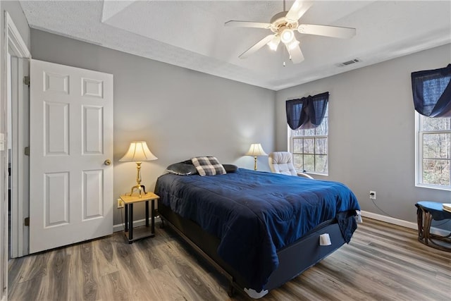 bedroom with baseboards, visible vents, ceiling fan, wood finished floors, and a textured ceiling