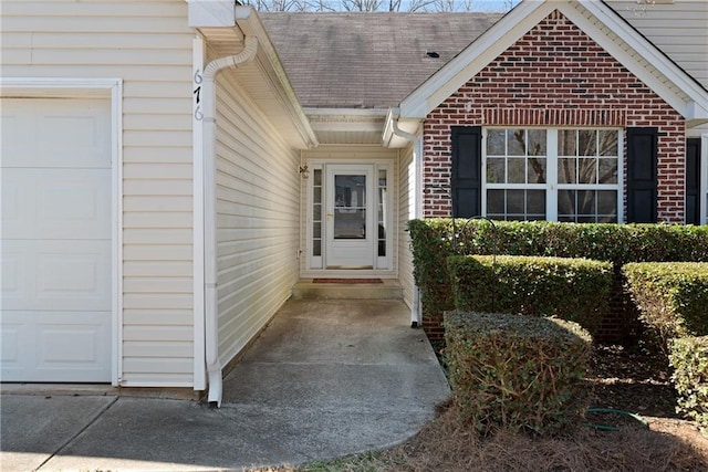 property entrance with brick siding, roof with shingles, and an attached garage