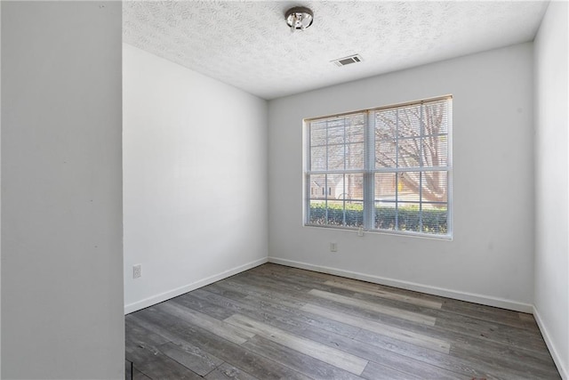 spare room featuring visible vents, a textured ceiling, baseboards, and wood finished floors