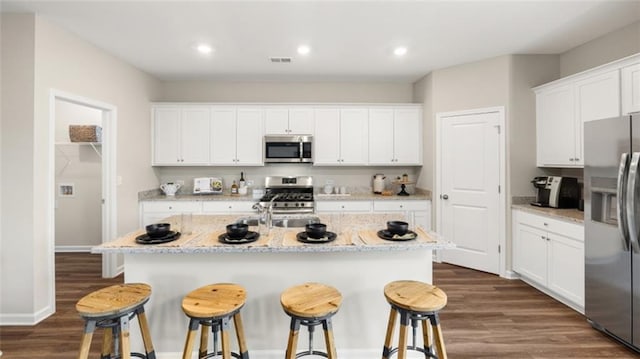 kitchen with dark hardwood / wood-style floors, stainless steel appliances, a breakfast bar area, and a kitchen island with sink