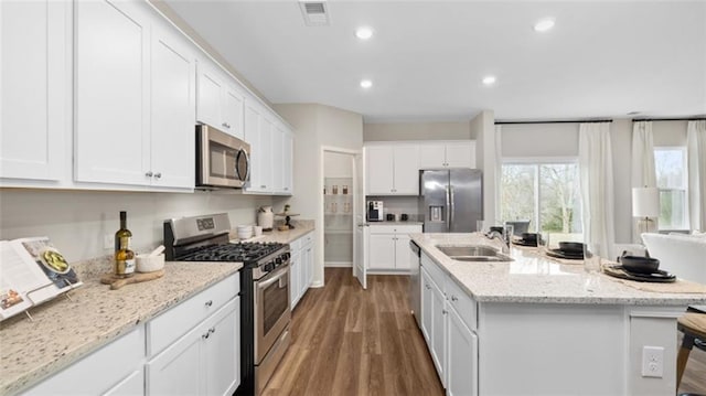 kitchen with white cabinetry, an island with sink, hardwood / wood-style floors, sink, and appliances with stainless steel finishes