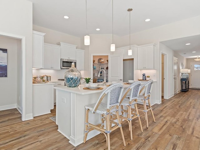 kitchen featuring a center island with sink, white cabinets, hanging light fixtures, and light hardwood / wood-style flooring