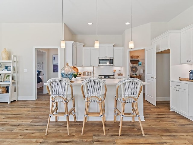 kitchen featuring pendant lighting, light hardwood / wood-style floors, white cabinetry, and a breakfast bar area