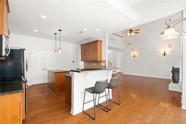 kitchen featuring tasteful backsplash, hardwood / wood-style flooring, appliances with stainless steel finishes, pendant lighting, and ceiling fan