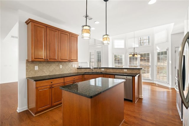 kitchen featuring pendant lighting, stainless steel appliances, a kitchen island, decorative backsplash, and kitchen peninsula