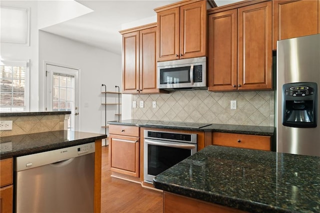 kitchen featuring stainless steel appliances, light wood-type flooring, decorative backsplash, and dark stone countertops