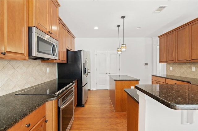 kitchen with tasteful backsplash, decorative light fixtures, a center island, light hardwood / wood-style flooring, and appliances with stainless steel finishes