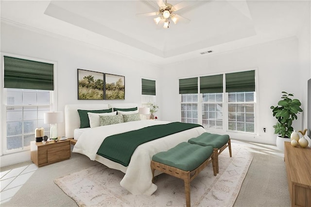 bedroom with multiple windows, light colored carpet, a raised ceiling, and ceiling fan