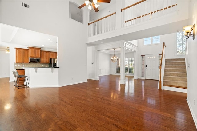 unfurnished living room featuring ornate columns, dark hardwood / wood-style flooring, ceiling fan with notable chandelier, and a high ceiling