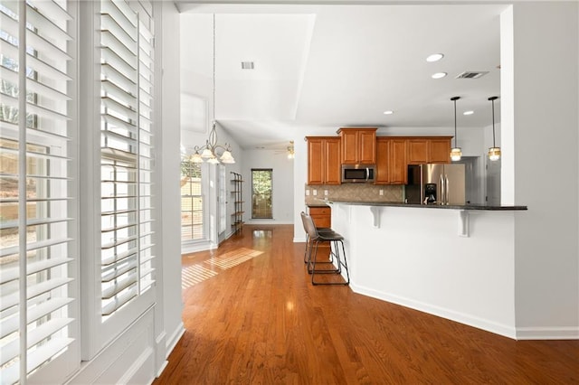 kitchen featuring a breakfast bar, kitchen peninsula, pendant lighting, stainless steel appliances, and decorative backsplash