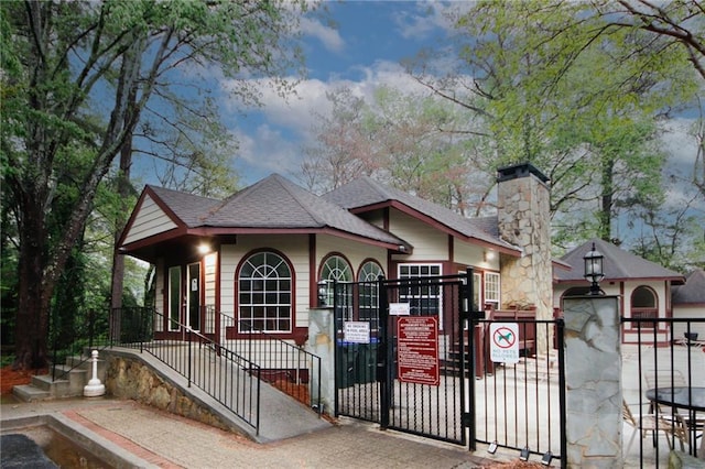 view of front of property featuring roof with shingles, a fenced front yard, a chimney, and a gate