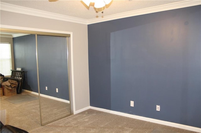 unfurnished bedroom featuring baseboards, ceiling fan, crown molding, carpet flooring, and a closet