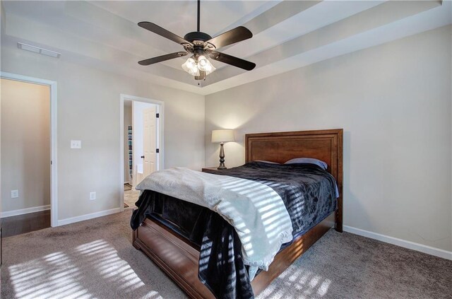 carpeted bedroom with ceiling fan and a tray ceiling