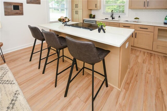 kitchen featuring sink, light brown cabinets, a breakfast bar, a kitchen island, and light wood-type flooring