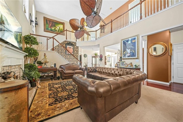 living area with a ceiling fan, wood finished floors, baseboards, a towering ceiling, and stairs