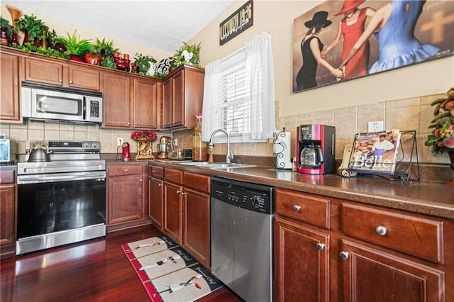 kitchen featuring dark wood-style flooring, a sink, stainless steel appliances, dark countertops, and backsplash