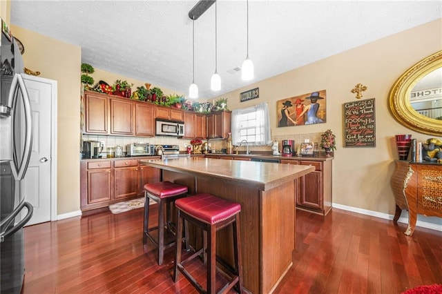 kitchen with dark wood-type flooring, a breakfast bar area, brown cabinetry, and stainless steel appliances