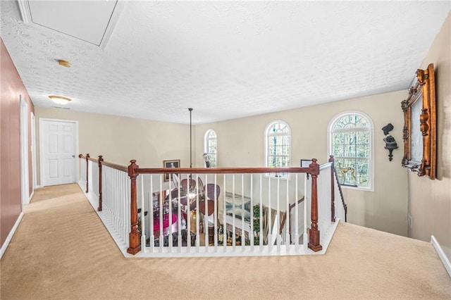 hallway featuring baseboards, attic access, a textured ceiling, carpet flooring, and an upstairs landing