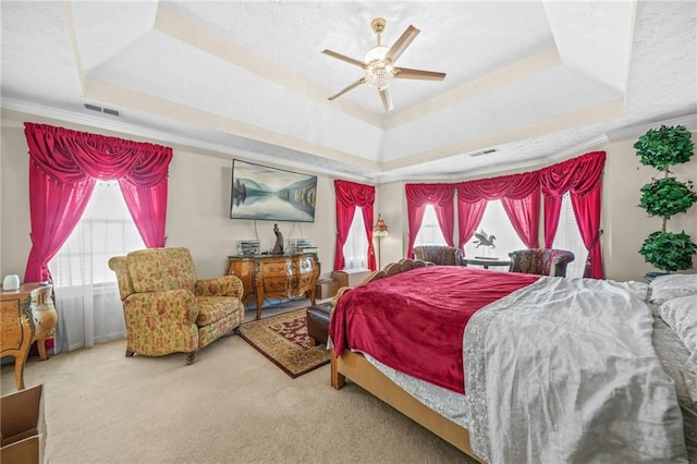 carpeted bedroom with a raised ceiling, multiple windows, crown molding, and visible vents