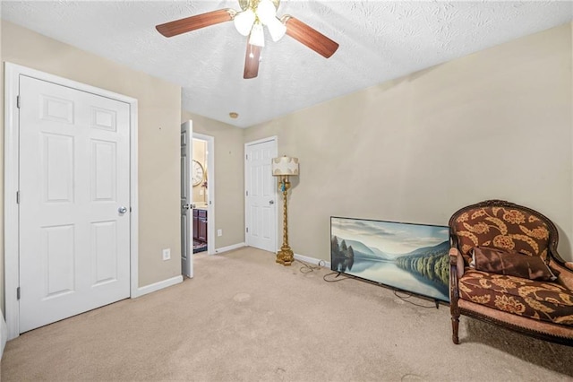 sitting room with baseboards, light colored carpet, a ceiling fan, and a textured ceiling