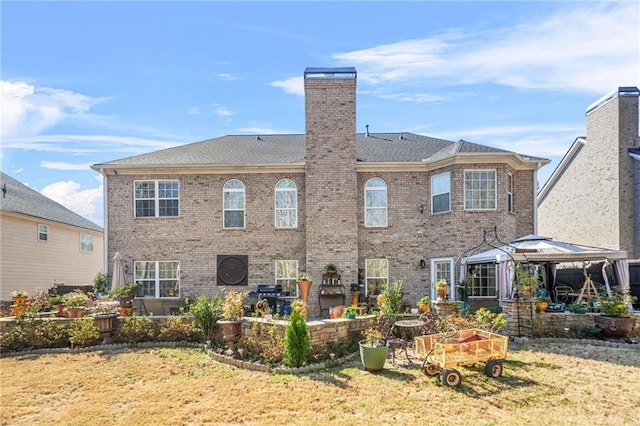 rear view of house featuring a gazebo, brick siding, a chimney, and a patio area