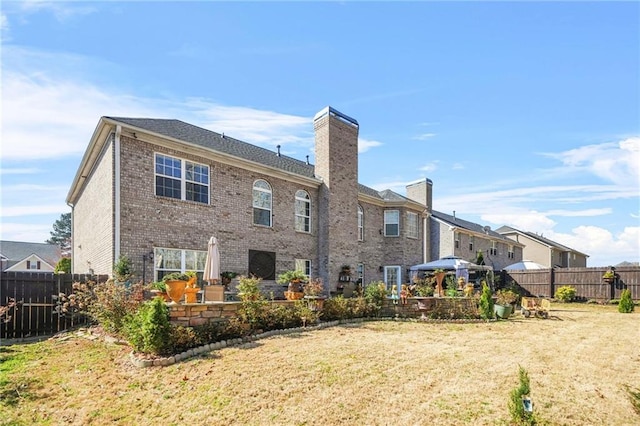 back of property with a patio, a fenced backyard, a yard, brick siding, and a chimney