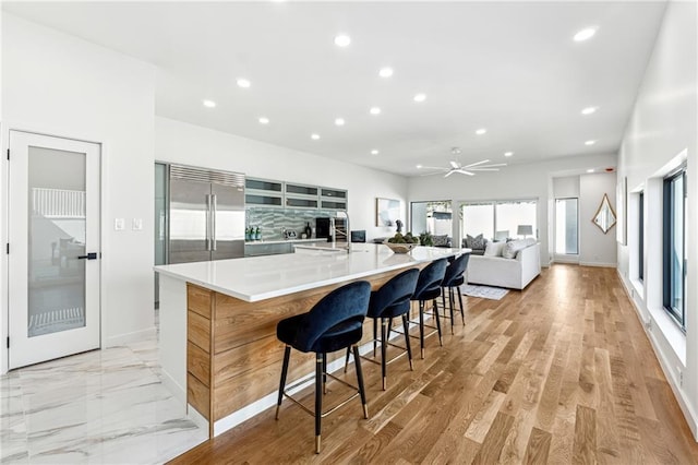 kitchen with built in fridge, recessed lighting, a sink, a large island, and light countertops