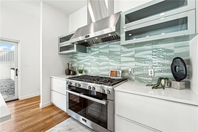 kitchen featuring high end stove, wall chimney range hood, white cabinetry, decorative backsplash, and light countertops