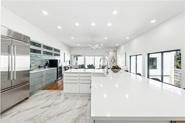 kitchen featuring light wood-type flooring, double oven range, wall chimney range hood, decorative backsplash, and white cabinets