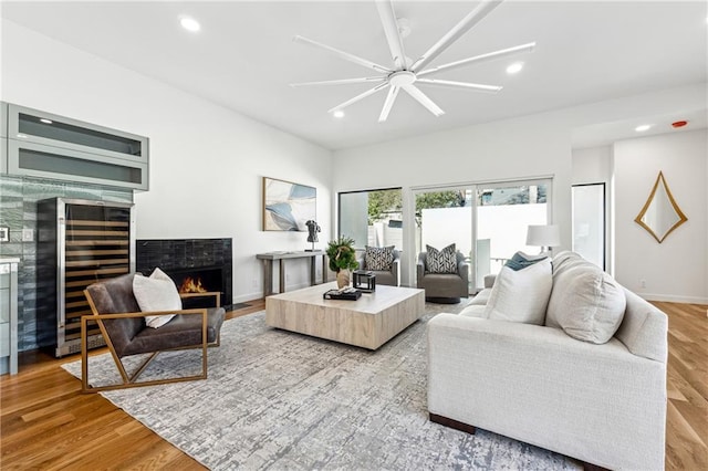 living area featuring beverage cooler, a lit fireplace, light wood-style floors, recessed lighting, and a ceiling fan