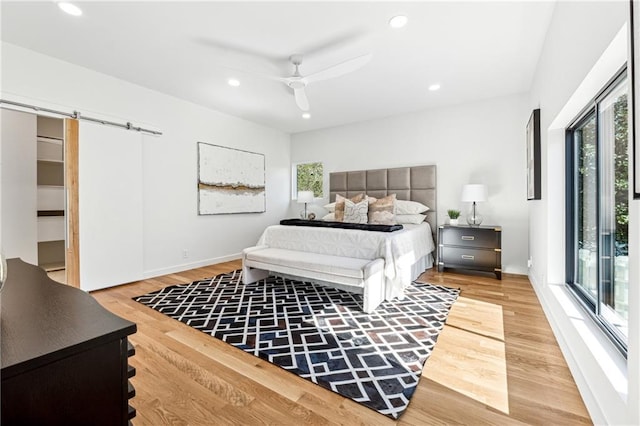bedroom with a barn door, light wood-style flooring, recessed lighting, ceiling fan, and access to exterior
