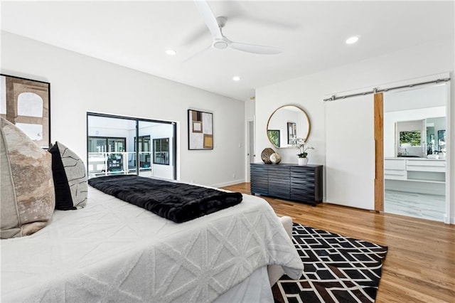 bedroom featuring wood finished floors, a barn door, recessed lighting, a ceiling fan, and ensuite bathroom