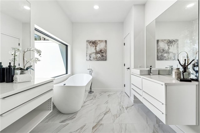 bathroom featuring a freestanding bath, vanity, recessed lighting, marble look tile flooring, and baseboards
