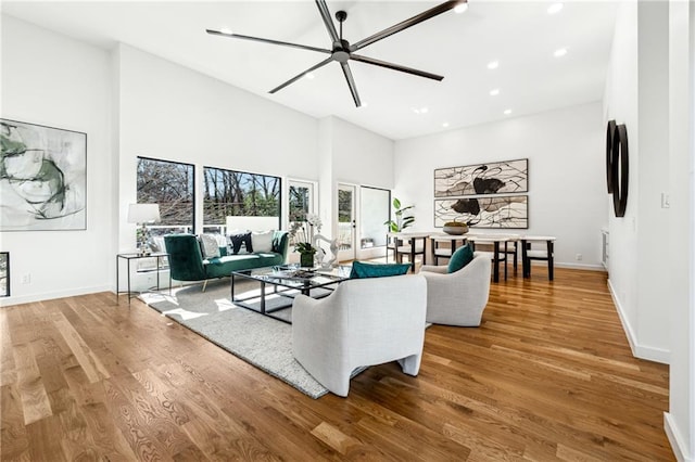 living room with wood finished floors, recessed lighting, a towering ceiling, and baseboards
