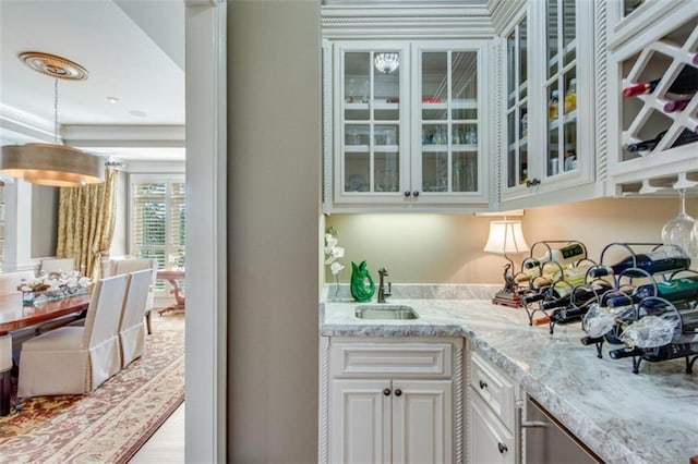 bar with light stone counters, sink, white cabinets, and light hardwood / wood-style floors