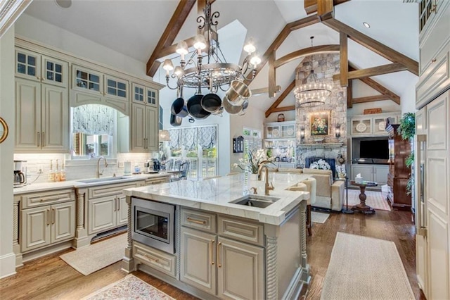 kitchen with a kitchen island with sink, sink, pendant lighting, high vaulted ceiling, and stainless steel microwave