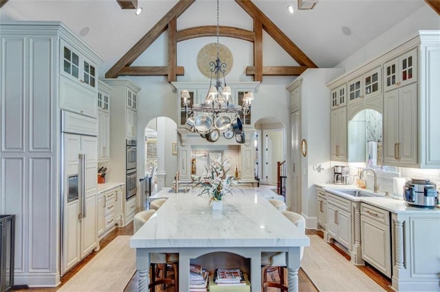 kitchen with pendant lighting, high vaulted ceiling, sink, light hardwood / wood-style flooring, and light stone counters