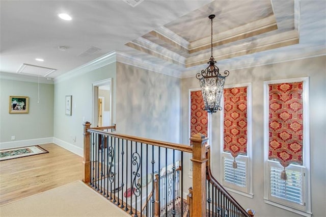 corridor with wood-type flooring, ornamental molding, and a tray ceiling