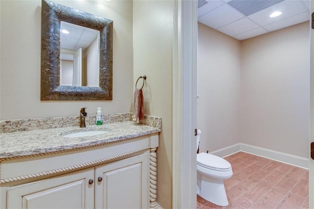 bathroom with hardwood / wood-style floors, vanity, a drop ceiling, and toilet