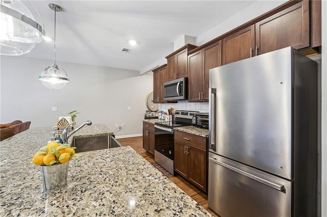 kitchen with light stone counters, dark wood-style flooring, decorative light fixtures, stainless steel appliances, and a sink