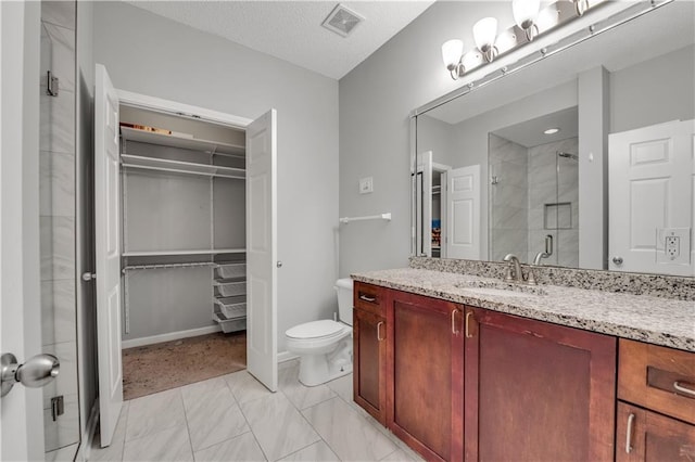 bathroom featuring vanity, toilet, a shower with shower door, and a textured ceiling