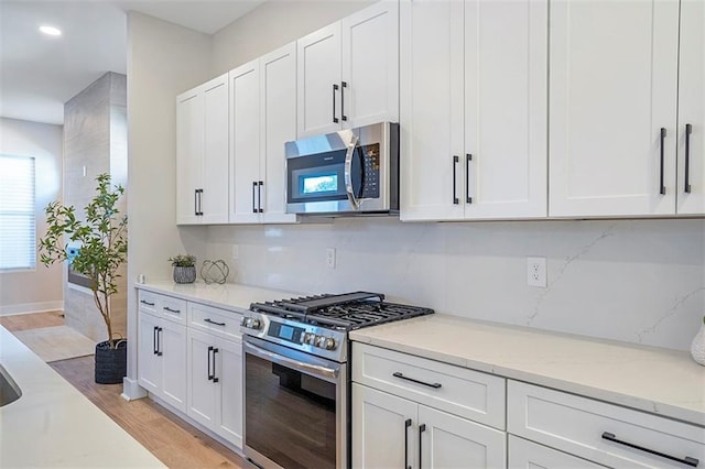 kitchen with stainless steel appliances, light wood-style floors, decorative backsplash, and white cabinetry