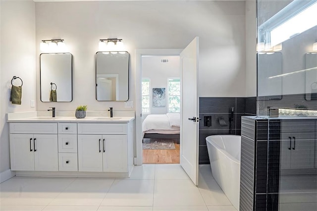 ensuite bathroom featuring a soaking tub, double vanity, tile patterned floors, and a sink