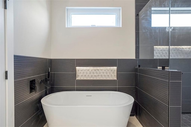 full bath featuring tiled shower, wainscoting, a freestanding bath, and tile walls