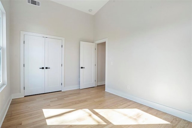 unfurnished bedroom with visible vents, baseboards, light wood-style floors, a closet, and high vaulted ceiling